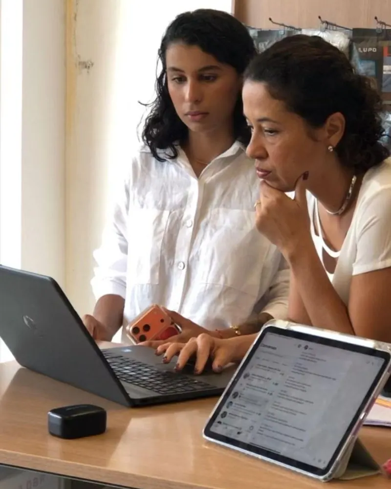 Duas pessoas observando um computador portátil em uma mesa com um tablet.